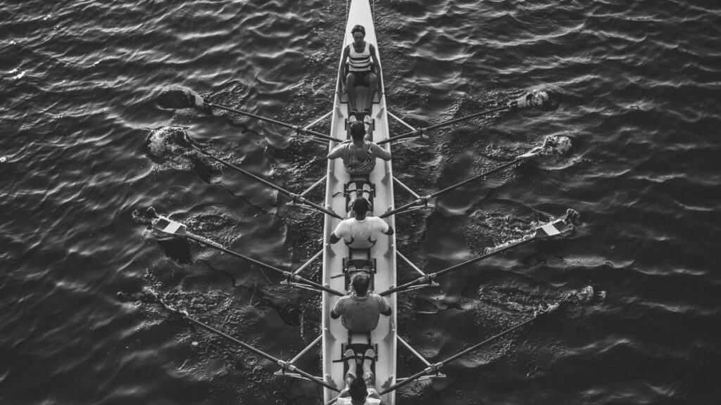 A rowing eight moving in sync seen from above, a metaphor for a team executing a shared strategy with coordinated effort