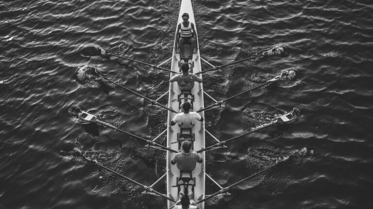 A rowing eight moving in sync seen from above, a metaphor for a team executing a shared strategy with coordinated effort